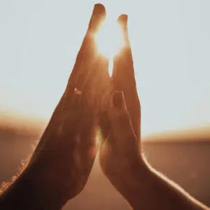 two hands are held up, almost touching. A bright light appears behind the hands, as if they are destined to soon touch.