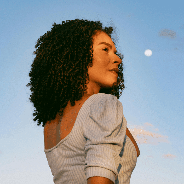 A black woman stands in front of the bright night sky, the Full Moon seen in the background.