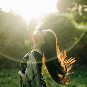 A woman reaches up into the sky as if she is grabbing the Sun.