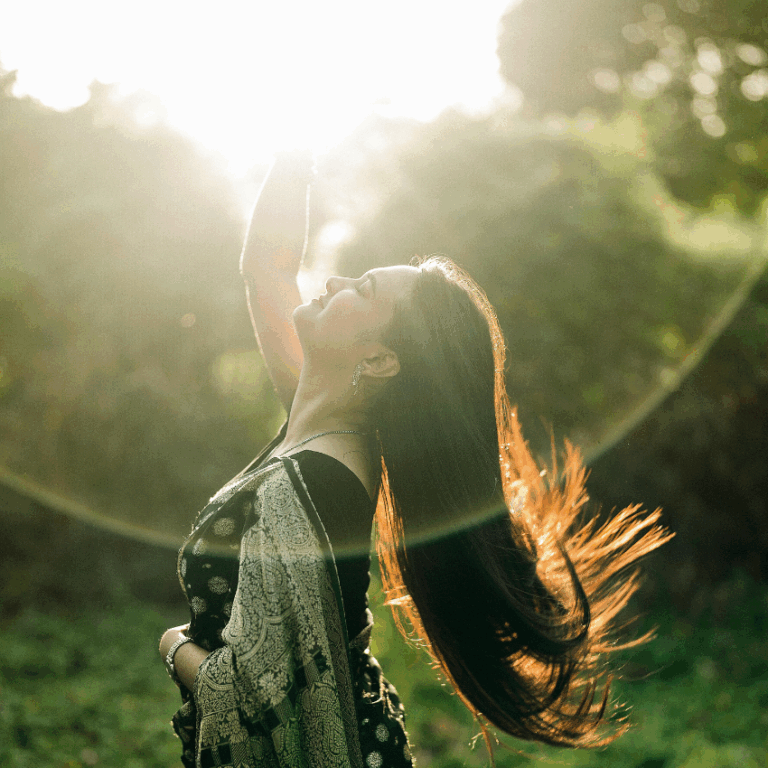 A woman reaches up into the sky as if she is grabbing the Sun.