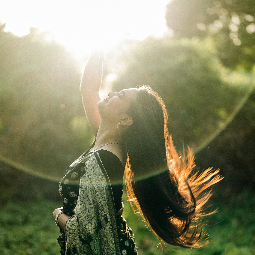 A woman reaches up into the sky as if she is grabbing the Sun.