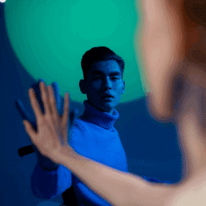 Two men hold one hand up, mirroring the other. One is bathed in a blue light.