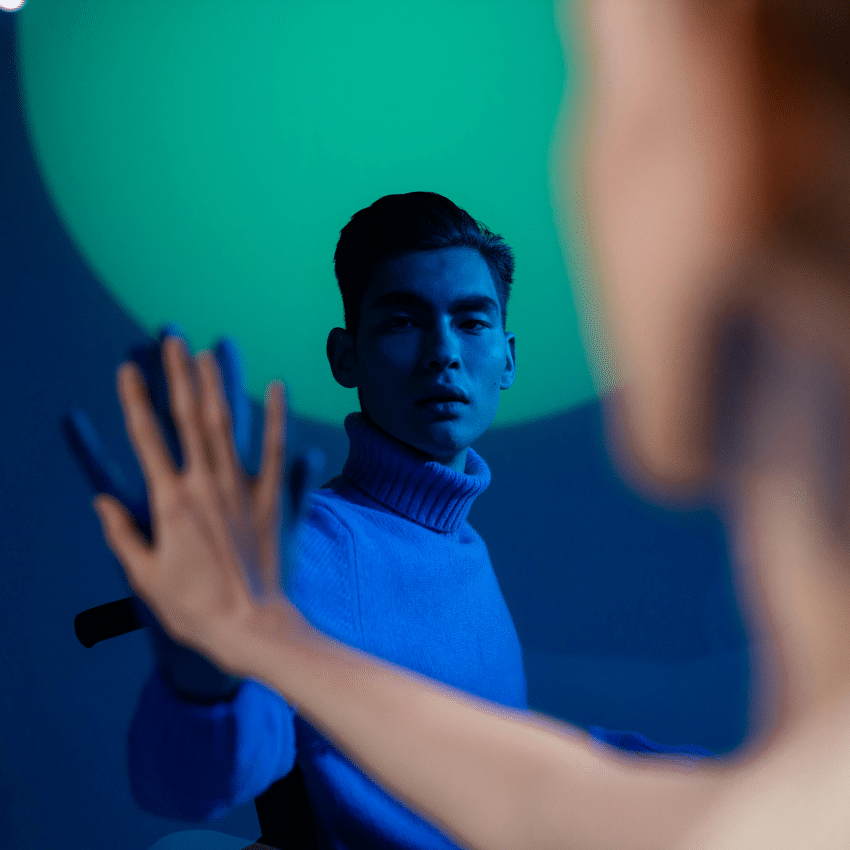 Two men hold one hand up, mirroring the other. One is bathed in a blue light.