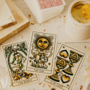 The Sun, The World, and the 2 of Cups Tarot cards lay on a table next to a candle with a yellow flower in it.