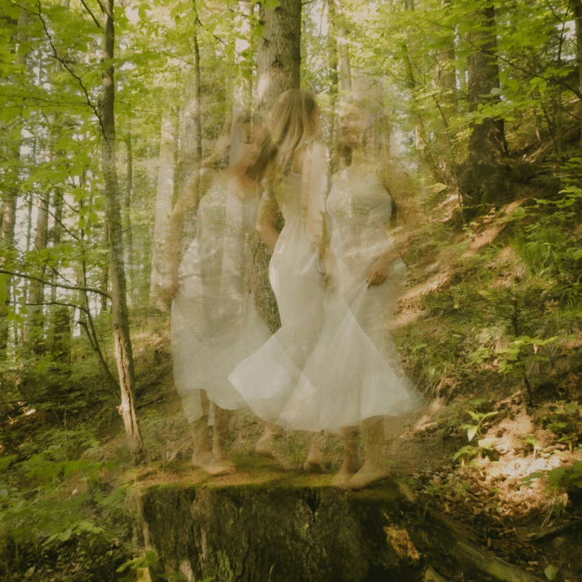 A blurry woman appears to be dancing on a woodcut in a forest.