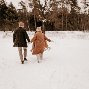A couple holds hands as they walk through the snow.