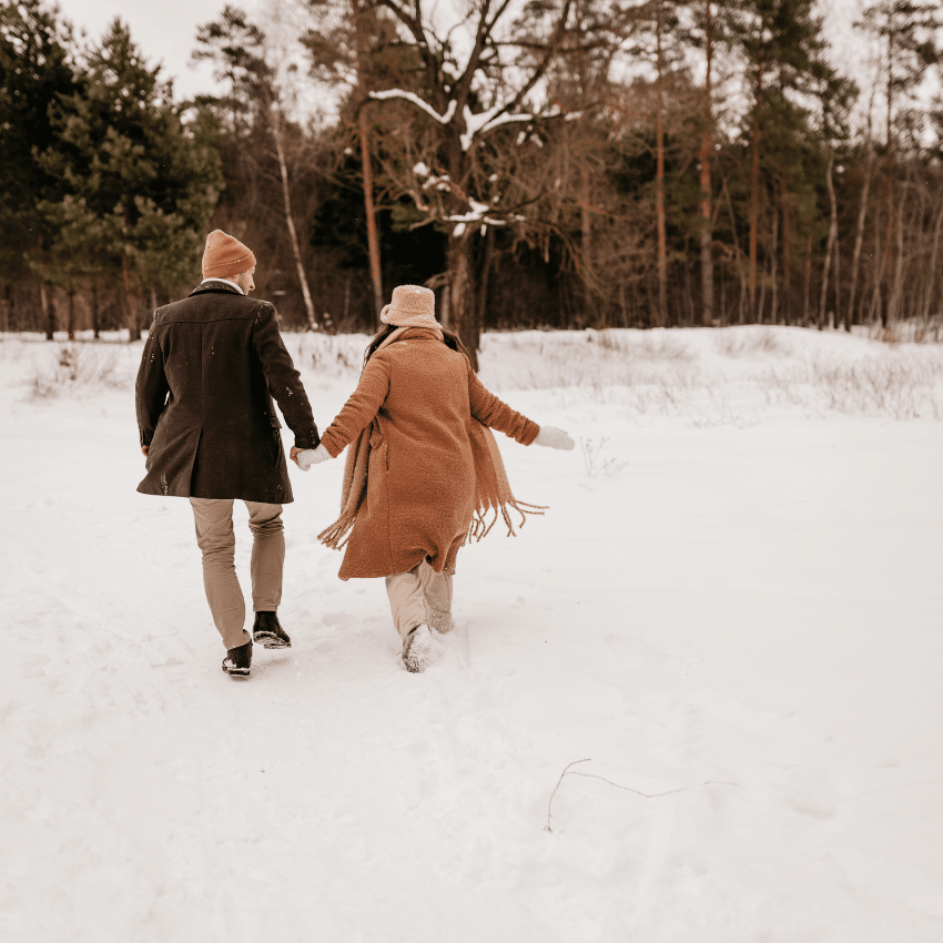 A couple holds hands as they walk through the snow.