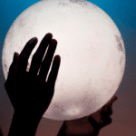 pair of hands holding up a glowing full moon