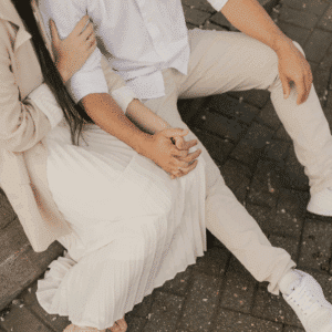 A couple wearing light-colored clothes holds hands. Their faces are not visible.