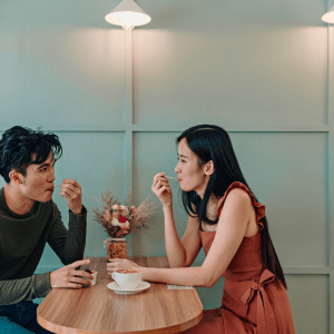 Asian couple sitting at a wooden table in a cafe enjoying coffee and ice cream