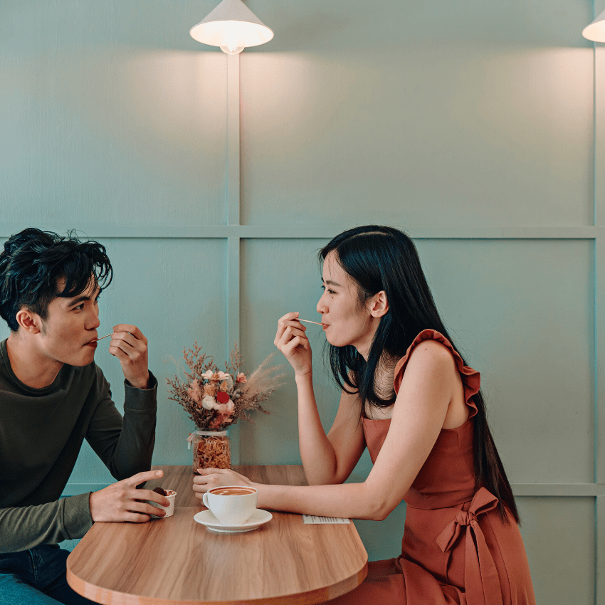 Asian couple sitting at a wooden table in a cafe enjoying coffee and ice cream