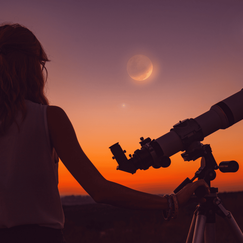 woman with a telescope gazing at a new moon in a purple and orange sky
