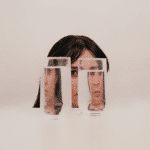A woman's face appears behind 2 glasses of water, the water distorts her image representing the energy of Jupiter retrograde in Cancer.