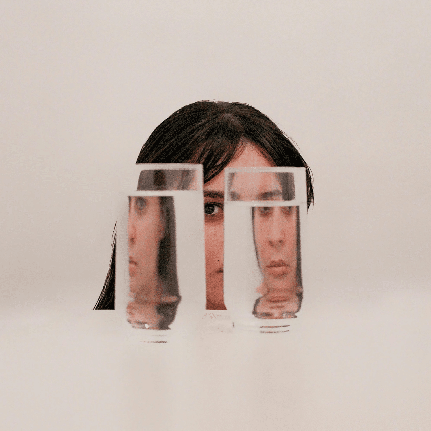 A woman's face appears behind 2 glasses of water, the water distorts her image representing the energy of Jupiter retrograde in Cancer.