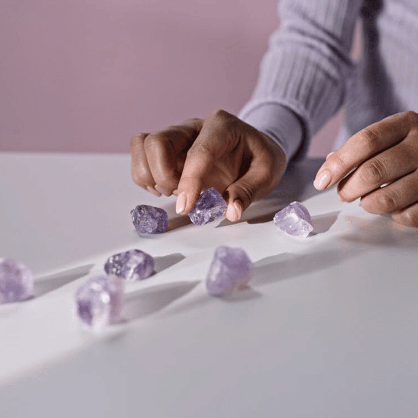 pair of hands organizing purple crystals on a white table