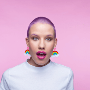 woman with short purple hair and rainbow earrings looking surprised