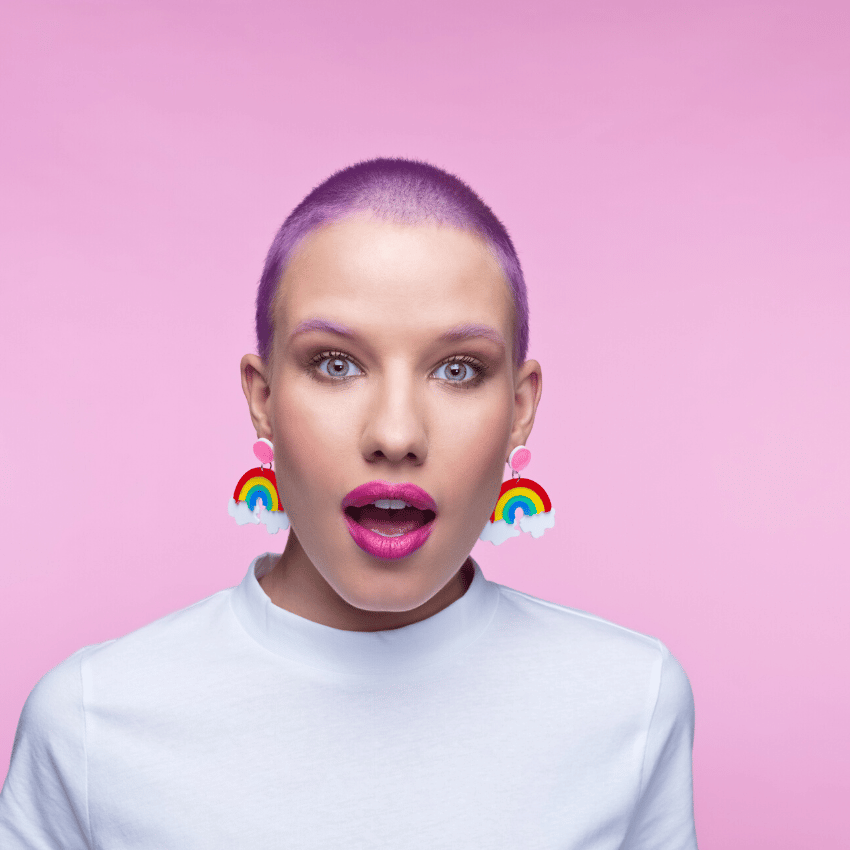 woman with short purple hair and rainbow earrings looking surprised