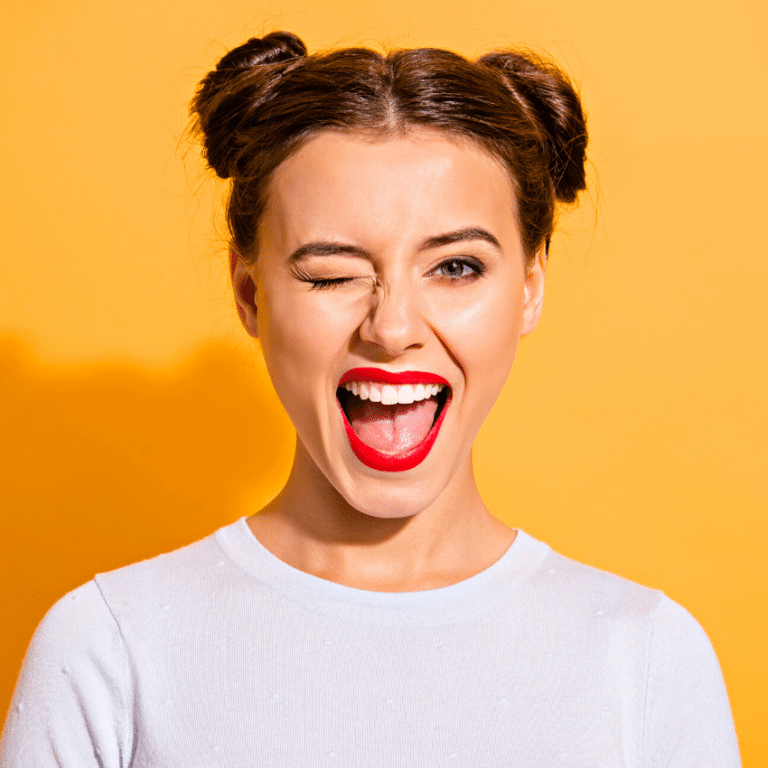 brunette woman with bright red lipstick against a yellow background winking and smiling