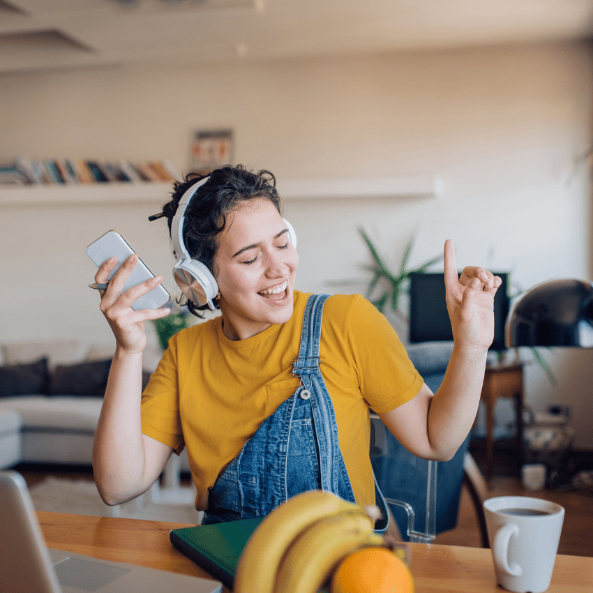 woman sitting at a dining room table with headphones on seemingly dancing to music