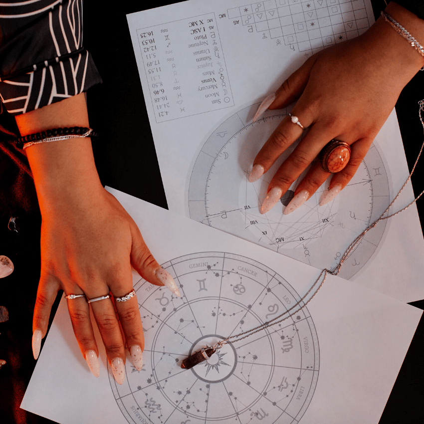 hands spread out over papers detailing astrological charts