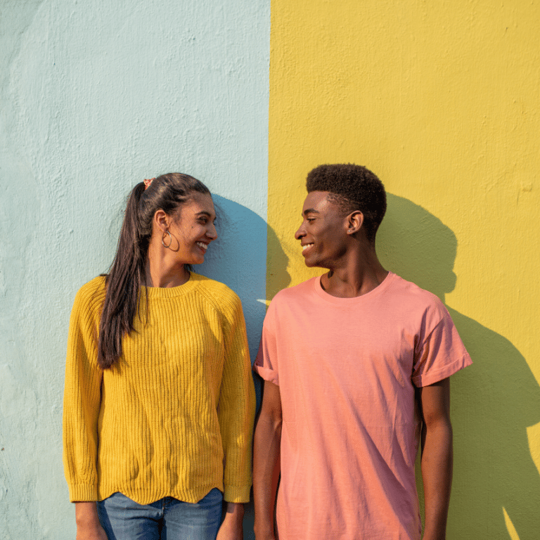 man and woman against a blue and yellow wall looking at each other and smiling