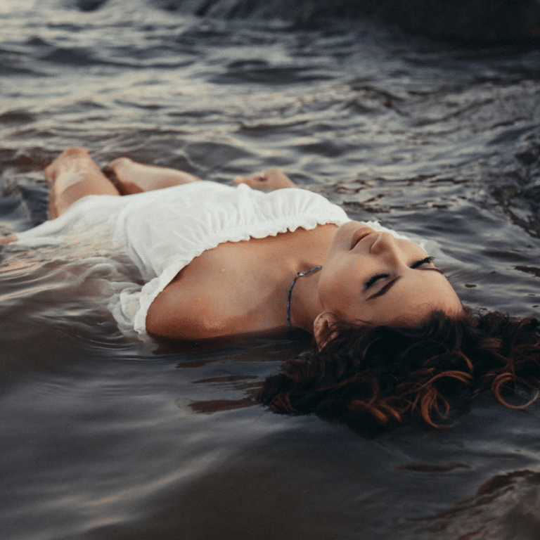 brunette woman in a white dress floating in water on her back