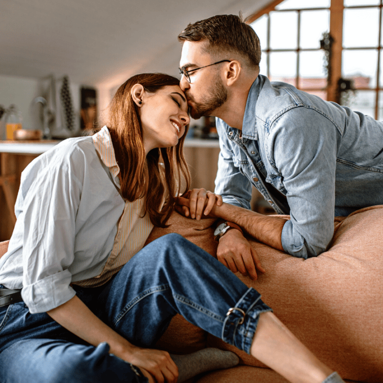 man kissing the forehead of a woman sitting on a couch