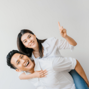 couple in white t-shirts smiling as the man gives the woman a piggyback ride