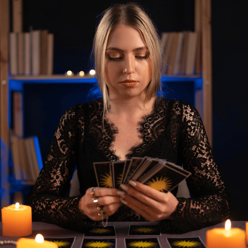 blonde woman reading tarot cards sitting at a table with orange candles