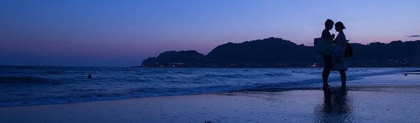 The beach and a rocky hill are bathed in purple and blue light.