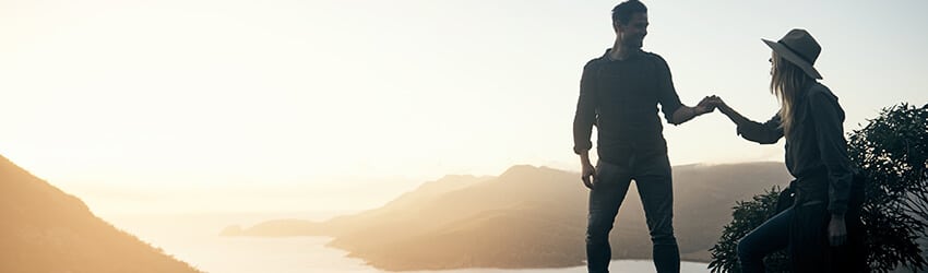 A silhouetted figure stands with a rocky hill in the background, bathed in morning light.