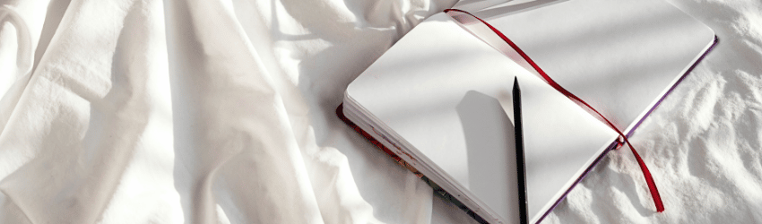 A blank journal sits on a bed with pen on the page.