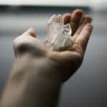 A hand with a clear quartz crystal is reaching out.