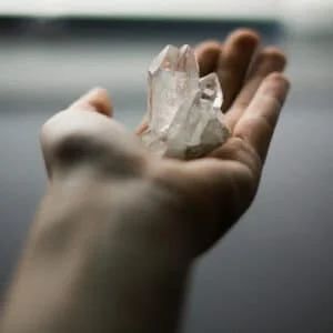 A hand with a clear quartz crystal is reaching out.