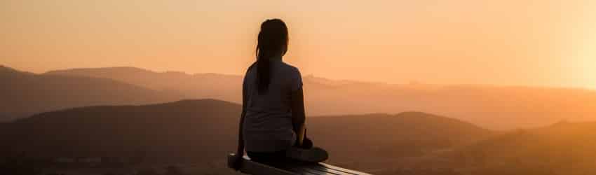 Une personne est assise et réfléchit en regardant un coucher de soleil orange.