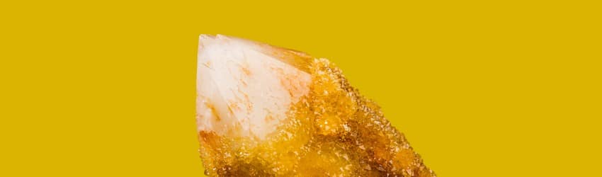 A yellow citrine crystal shard pointing towards the top left of the image on an orange background.