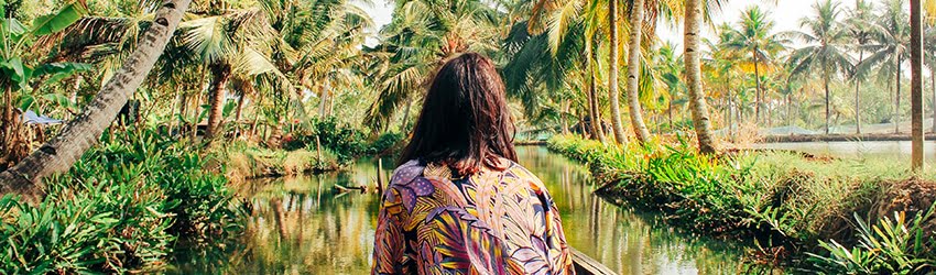 A woman in a colorful top faces a small body of water in the jungle.