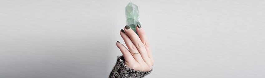 A Virgo woman holds up a green quartz crystal point in her hands.