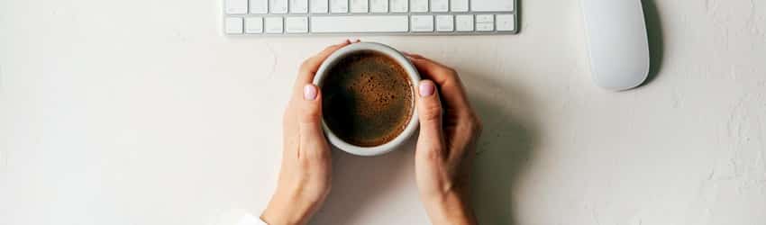 hands on desk holding a coffee cup