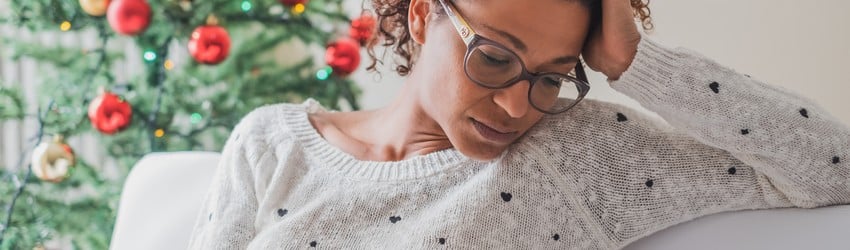 woman-on-couch-looking-stressed-out-with-a-christmas-tree-behind-her