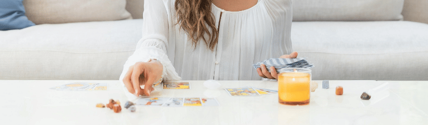 A woman wearing all white looks upon the Tarot cards spread in front of her.