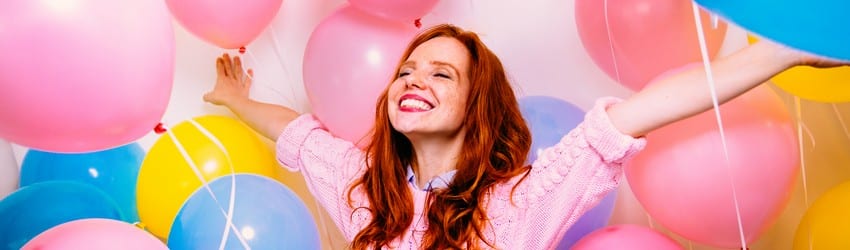redheaded woman surronded by balloons smiling