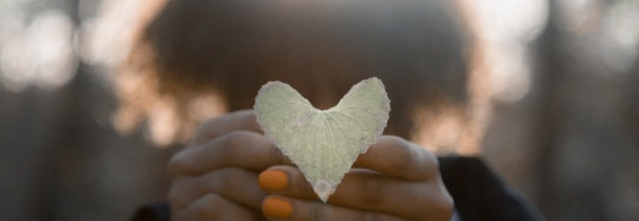 A person holds a heart out in front of their face.
