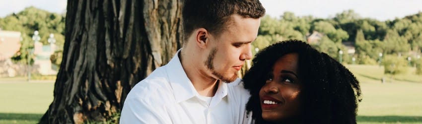 A couple looks at each other with love in their eyes while the sit under a tree.