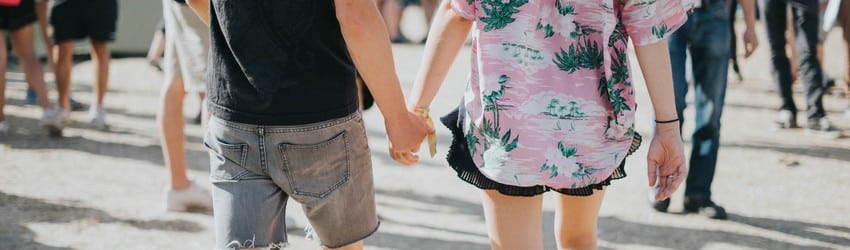 Two people walking in a crowd of people near the boardwalk holding hands.