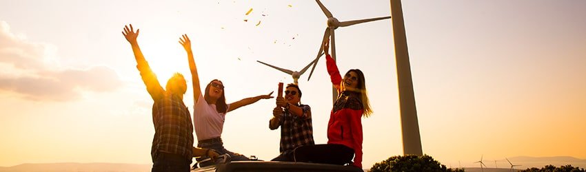 Four friends sit in the sun in front of wind turbines.