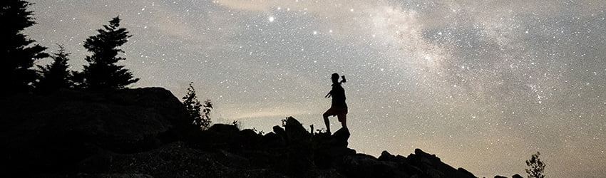 A person is climbing a hill in front of a grey colored starry sky.