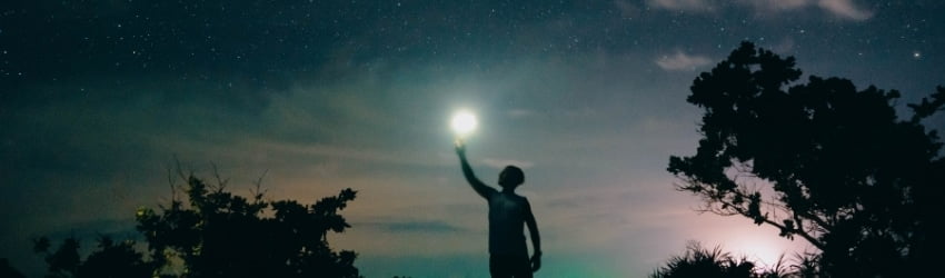 A man holds a flashlight up to the sky.