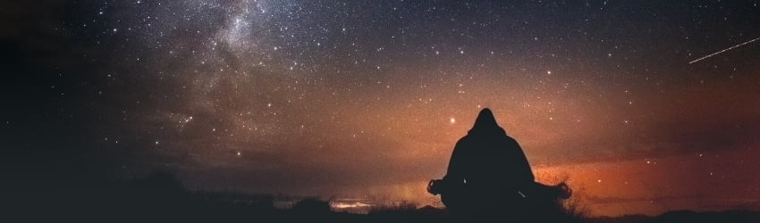 A person meditates against a galaxy sunset.