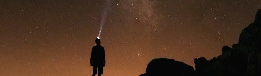 A man with a headlight stands under an orange starry sky.